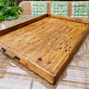 May include: A large, rectangular wooden serving tray with a natural wood finish and a black metal handle. The tray is made of reclaimed wood and has a rustic look.