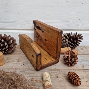 May include: A rustic wooden phone stand with a natural brown finish. The stand has a unique design with a raised back and a cutout for holding a phone. The stand is perfect for adding a touch of rustic charm to any home.