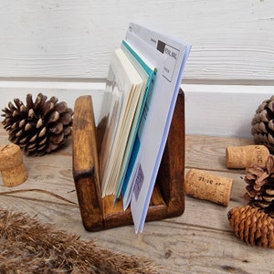 May include: A wooden letter holder with a dark brown stain. The holder has two slots for mail or papers. The holder is sitting on a wooden surface with pine cones and cork stoppers.