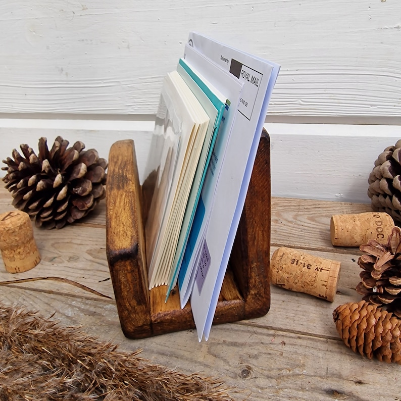 May include: A wooden letter holder with a dark brown stain. The holder has two slots for mail or papers. The holder is sitting on a wooden surface with pine cones and cork stoppers.