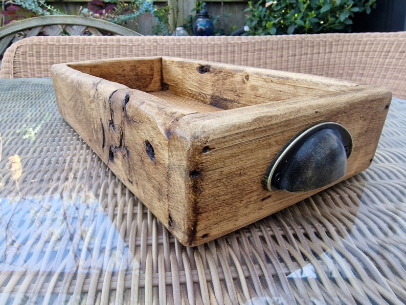 May include: A rustic wooden tray with a dark brown metal handle. The tray is made of reclaimed wood and has a natural finish.