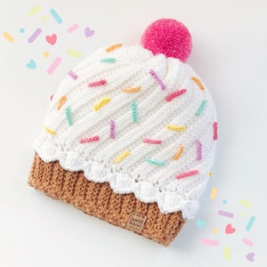 May include: White crocheted cupcake hat with colorful sprinkles and a brown brim. The hat has a pink pom pom on top and a brown label that says "Sweet Berries" on it.