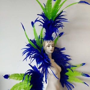 May include: A blue and green feather headdress with a large plume of blue feathers and smaller green feathers. The headdress is worn on a white mannequin.