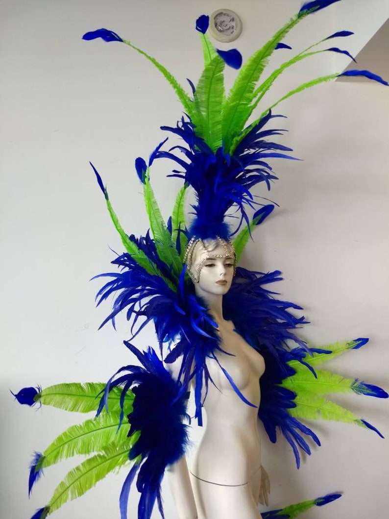 May include: A blue and green feather headdress with a large plume of blue feathers and smaller green feathers. The headdress is worn on a white mannequin.