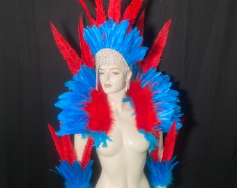 Puede incluir: Un vibrante conjunto de disfraz de carnaval que incluye un tocado alto y elaborado con plumas de color rojo brillante y azul, una pieza de hombro de plumas a juego y brazaletes. El tocado incluye una banda plateada con incrustaciones de pedrería.