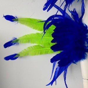 May include: A blue and green feather arm band with a black elastic band. The arm band is made of feathers and is designed to be worn on the arm.