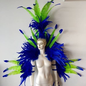 May include: A blue and green feather headdress and shoulder piece. The headdress is tall and features a large plume of blue feathers with green feathers extending out from the sides. The shoulder piece is a pair of blue feather wings that are attached to the headdress.
