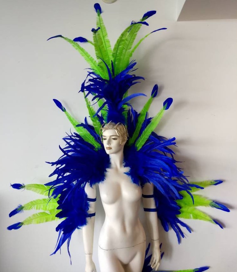 May include: A blue and green feather headdress and shoulder piece. The headdress is tall and features a large plume of blue feathers with green feathers extending out from the sides. The shoulder piece is a pair of blue feather wings that are attached to the headdress.
