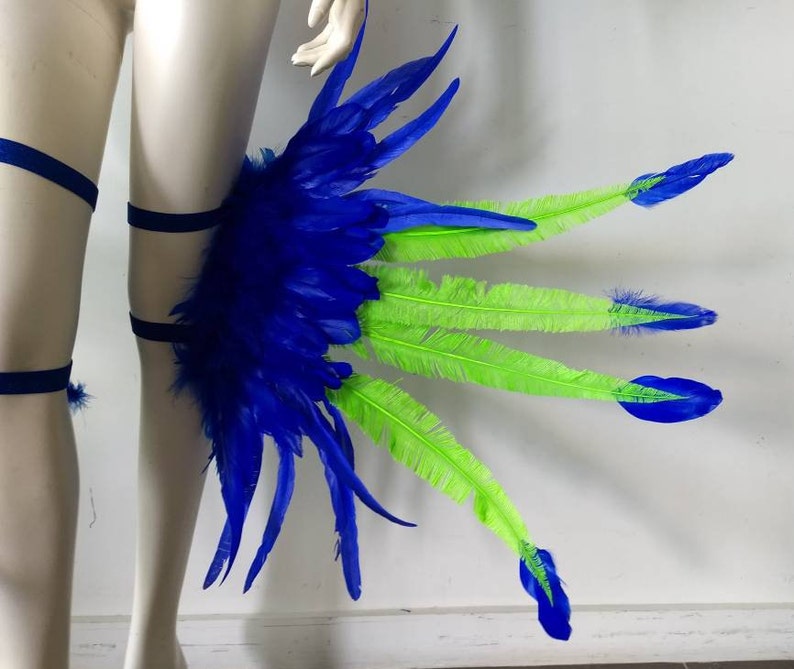 May include: Blue and green feather leg piece with black elastic straps. The feathers are arranged in a fan shape with the blue feathers on the inside and the green feathers on the outside.