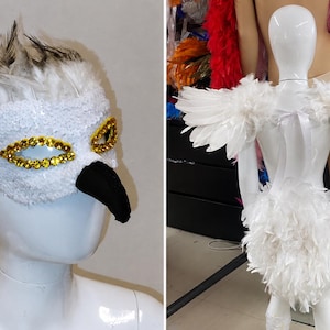 Può includere: Una maschera da uccello in piume bianche con dettagli in paillettes dorate intorno agli occhi e un becco nero, abbinata a un set di ali in piume bianche. La maschera presenta piume bianche con punte grigie sulla parte superiore.