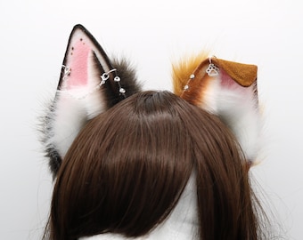 May include: Faux fur cat ears in black, white, brown, and tan. The ears have pink inner details and are decorated with silver chains and rhinestones. One ear has a paw print charm.