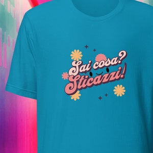 May include: A turquoise blue t-shirt with a pink and yellow graphic design that says "Sai cosa? Sticazzi!" with a cartoon smiley face.