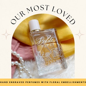 May include: A clear glass bottle of perfume with a white cap and a floral design. The bottle is engraved with the word "Bride" and the date "9.29.23". The bottle is sitting on a yellow and pink fabric background.