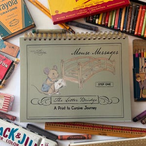 May include: A spiral-bound workbook titled Mouse Messages: The Letter Bridge, A Print to Cursive Journey, featuring a mouse illustration and a wooden bridge. It is surrounded by vintage crayon boxes, colored pencils, a wooden ruler, and paint sets.