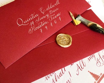 Può includere: Una busta rossa con calligrafia bianca che recita "Quintin Caldwell, 14 Snowy Drive, Houston, Texas 74101". La busta ha un sigillo di cera dorato ed è appoggiata su una superficie bianca con un foglio di carta bianco che recita "we shall soon! All my love".