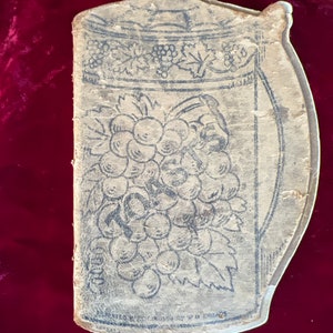 May include: A vintage, cream-colored, paperboard,  rectangular,  shaped like a pitcher,  with a black and white illustration of a bunch of grapes and leaves. The text "UNITED STATES PATENTED" is visible at the bottom.