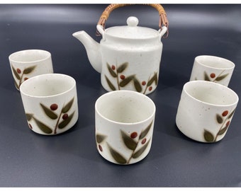 May include: A white ceramic teapot with a brown wicker handle and a floral design, along with six matching teacups.
