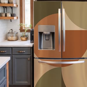 May include: A French door refrigerator featuring a large-scale geometric pattern in shades of olive green, burnt orange, and cream. The appliance includes a central water and ice dispenser on the left door and a horizontal handle on the bottom freezer drawer.