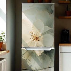 May include: A tall, upright refrigerator featuring a large, soft-focus floral graphic across its front panels. The design displays oversized, layered white and pale green petals with delicate gold-toned outlines, creating a smooth, artistic finish.