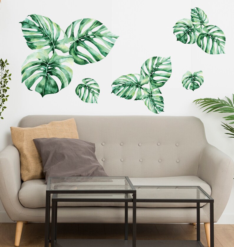 You can see that monstera wall decal set make living room jungle theme decorated. Large Watercolor Monstera Wall Decals, Monstera leaf, Tropic leaves decal, Tropical plants decal. The photo describe large watercolor monstera wall decals above sofa.