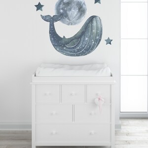 Pu&ograve; includere: Una cassettiera bianca con sei cassetti e un piano per il cambio. Una balena con una luna in bocca e stelle sono sul muro dietro la cassettiera.