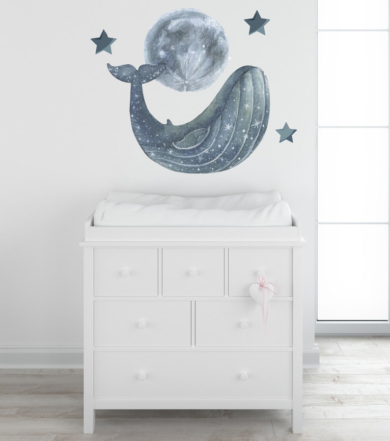 Pu&ograve; includere: Una cassettiera bianca con sei cassetti e un piano per il cambio. Una balena con una luna in bocca e stelle sono sul muro dietro la cassettiera.