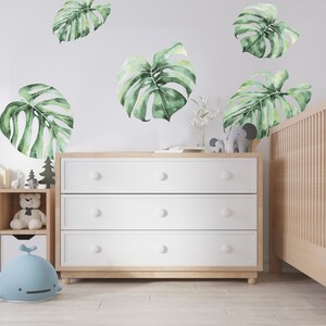 Jungle themed nursery you see on the photo. Monstera leaves wall decals are sticked above crib in the baby room nursery.