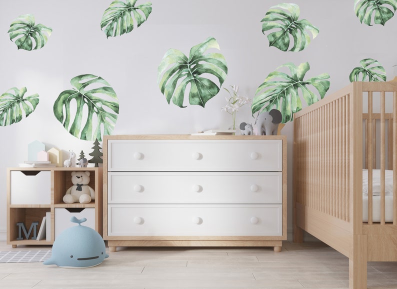 Jungle themed nursery you see on the photo. Monstera leaves wall decals are sticked above crib in the baby room nursery.
