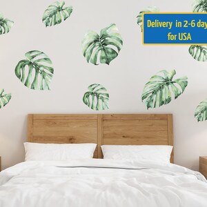 May include: A white bed with a wooden headboard and a white duvet cover. The wall behind the bed is white and has several green monstera leaf decals. The text "Delivery in 2-6 days for USA" is printed on a blue rectangle at the top of the image.
