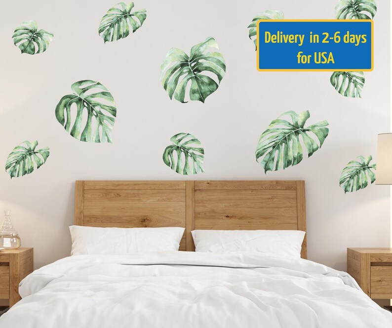 May include: A white bed with a wooden headboard and a white duvet cover. The wall behind the bed is white and has several green monstera leaf decals. The text "Delivery in 2-6 days for USA" is printed on a blue rectangle at the top of the image.