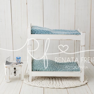 May include: White wooden bunk bed with a blue and white patterned mattress. The bed is on a white wooden floor with a white crocheted rug. A small white table with a laptop, a blue alarm clock, and a pair of glasses is in the foreground.