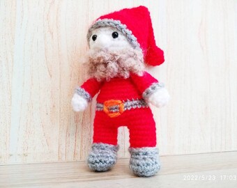 May include: A handmade crochet Santa Claus doll. The doll is dressed in a red suit with a matching hat, gray boots, and a gray and orange belt. It has a white face and a fluffy gray beard. A festive holiday decoration.