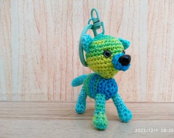 May include: A crocheted green, blue, and white wolf keychain with black eyes and a black nose.