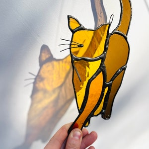 May include: A stained glass cat figurine with a yellow and orange color scheme. The cat is depicted with its tail raised in the air.