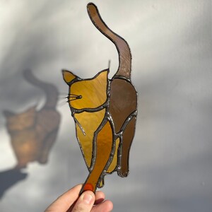 May include: A stained glass cat figurine with brown and yellow glass pieces. The cat is standing on its hind legs with its tail raised in the air.