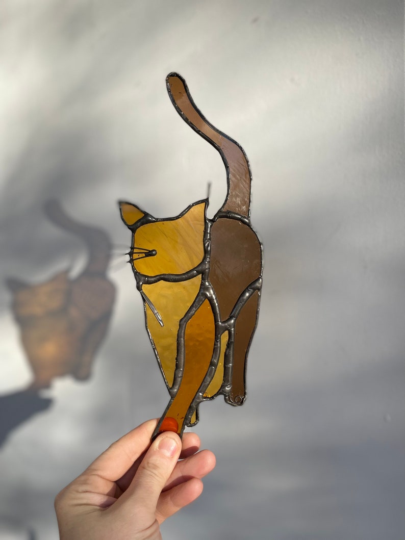 May include: A stained glass cat figurine with brown and yellow glass pieces. The cat is standing on its hind legs with its tail raised in the air.