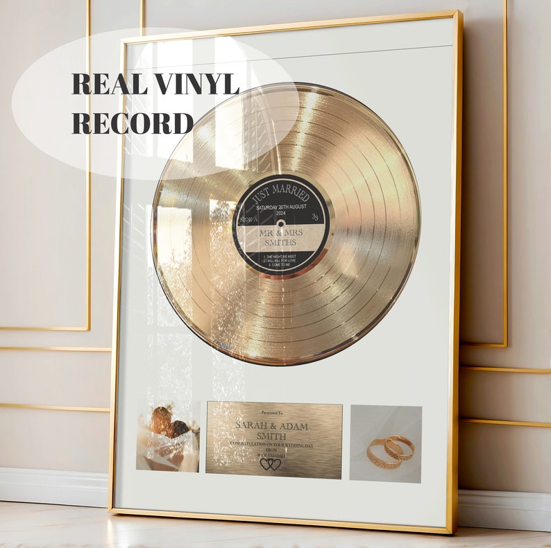 May include: A gold-coloured vinyl record framed in a gold frame. The record has a black label with the text "Just Married" and "Mr & Mrs Smiths". The frame also includes a small photo of a wedding couple and a pair of gold wedding bands.