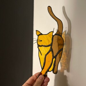 May include: A stained glass cat figurine with a yellow and brown color scheme. The cat is in a sitting position with its tail raised in the air.