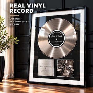 Puede incluir: Un cuadro decorativo con un disco de vinilo plateado metálico centrado sobre dos paneles rectangulares. La etiqueta del disco dice Happy Anniversary, Marc & Amanda, Amazed by Lonestar, 15th July 2017. Debajo, una placa dice Presented to Mrs & Mr Khambay.