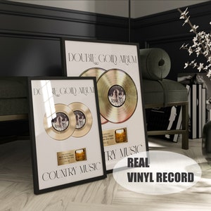 May include: Two gold records framed in black frames with the text "Double Gold Album" and "Country Music". The records are for the artist "Anna-Lee". The text "Real Vinyl Record" is in a white oval on a wood floor.