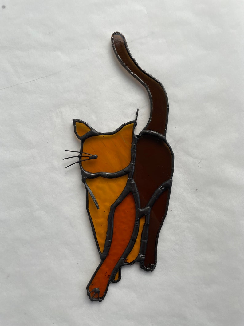 May include: A stained glass cat figurine with a brown tail and orange and yellow body.