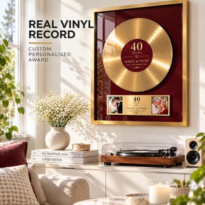 May include: A framed gold vinyl record award with a deep red background, featuring the text 40 YEARS, MARTA & PETER, and 14TH SEPTEMBER 1993. Below the record are two rectangular photo frames with the same text and date, all encased in a gold frame.