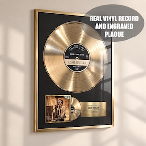 Op de afbeelding: Een ingelijste gouden vinylplaat met een centraal zwart label met de tekst Thank You, River Stone Band en Adam Singler. Daaronder bevindt zich een vierkante foto van een muzikant en een gegraveerd gouden plaatje met tekst.