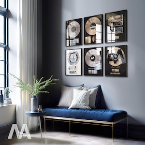 May include: A living room with a grey wall and a blue sofa. There are six framed records on the wall, each with a different design. The records are all silver and have a black border. The sofa is a dark blue and has a gold metal frame. There is a small table in front of the sofa with a vase of green plants on it.