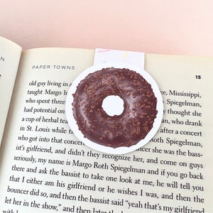 May include: A chocolate doughnut with sprinkles on top. The doughnut is on a white background with text that reads "Paper Towns" and "old guy living in a".