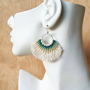 Puede incluir: Un par de pendientes de macramé verde, blanco y beige con un aro plateado y flecos.