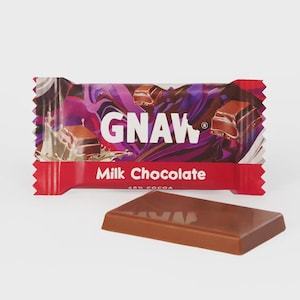 May include: A rectangular milk chocolate bar in a red, purple, and black wrapper with the text GNAW and Milk Chocolate 40% cocoa printed on the front. A single smooth, light brown milk chocolate piece is positioned in front of the wrapper.