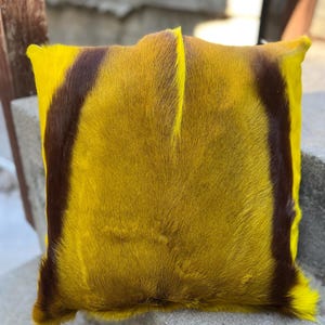May include: A yellow and brown fur throw pillow with a soft, fuzzy texture. The pillow is made of animal hide and has a unique, natural pattern.