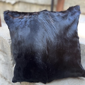 May include: Black cowhide pillow with a soft, plush texture. The pillow is made from real cowhide and has a natural, rustic look.