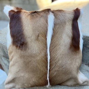 May include: A brown and white fur pillow with a white stripe down the center. The pillow is made from real animal hide and has a soft, plush texture.